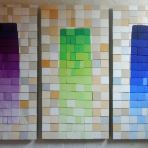 A triptych of three tiled waterfalls surrounded by off-white and beige tiles.  On the left is a purple fall, in the center a green waterfall, and on the right a blue waterfall. The Shingles Series is mixed-media; paint on PVC plastic and steel.
