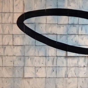 An abstract image painted on tiles; on the left we have a black area of tiles about 1/4 of the area then a large black halo floating in a background of off-white and grey tiles.