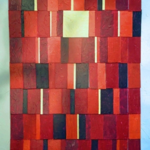An abstract tiled mixed media piece in various sheds of red black and pale yellow.