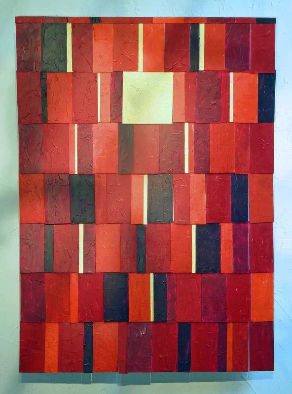 An abstract tiled mixed media piece in various sheds of red black and pale yellow.