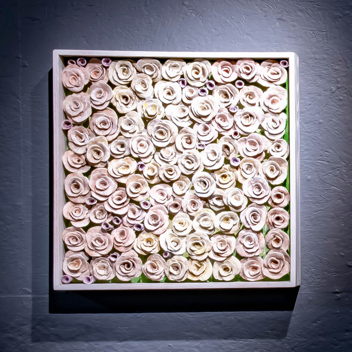 The Amulet Series 11 is a 26”x26” framed wooden box of low fired hand crafted clay roses in off white and pale pastels.
