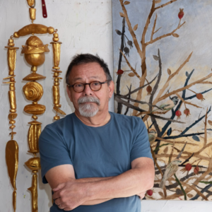 Photo of Oklahoma born multi-media artist Paul Medina standing in front of two of his pieces.