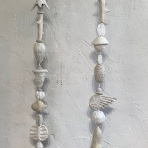 Picture of two strands of white and off white low fired clay objects hung from a steel rod  in Oklahoma born mixed-media artist Paul Medina's studio.