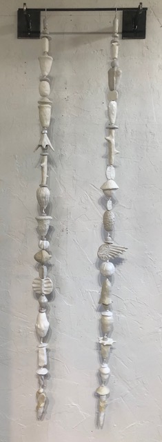 Picture of two strands of white and off white low fired clay objects hung from a steel rod  in Oklahoma born mixed-media artist Paul Medina's studio.