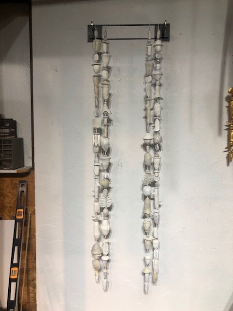 A picture of four strands of white and off-white low fired clay objects hung from a steel rod in Oklahoma born mixed-media artist Paul Medina's studio.