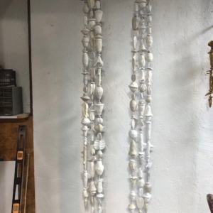 A picture of six strands of white and off-white low fired clay objects hung from a steel rod in Oklahoma born mixed-media artist Paul Medina's studio.