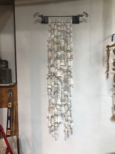 A picture of eight strands of white and off-white low fired clay objects hung from a decorative steel rod in Oklahoma born mixed-media artist Paul Medina's studio.