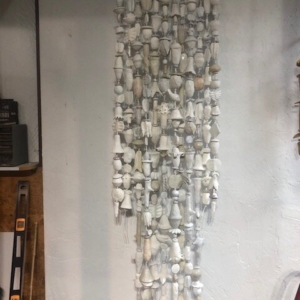 A picture of 12 strands of white and off-white low fired clay objects hung from a decorative steel rod in Oklahoma born mixed-media artist Paul Medina's studio.