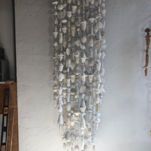 A picture of 12+ strands of white and off-white low fired clay objects hung from a decorative steel rod in Oklahoma born mixed-media artist Paul Medina's studio.