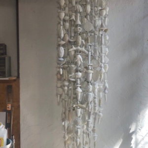 A picture of 16+ strands of white and off-white low fired clay objects hung from a decorative steel rod in Oklahoma born mixed-media artist Paul Medina's studio.