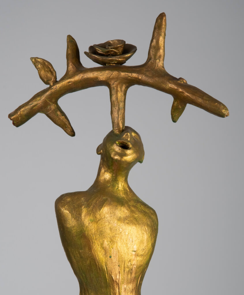 Penance is a mixed-media sculpture by Oklahoma born artist, Paul Medina. Penance is a golden human figure balancing a large branch on its head with several thorns and a rose on a green wooden base.