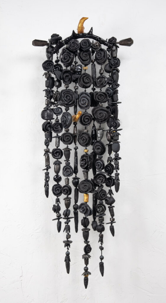 A mostly black mixed-media hanging wall amulet with clay objects