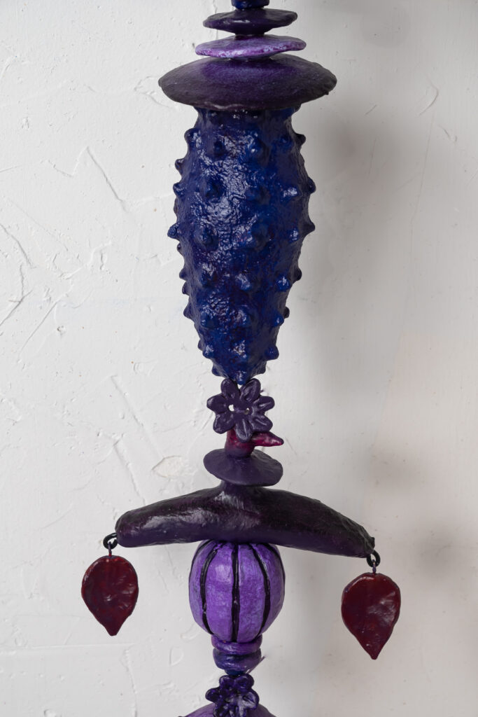 Close-up of "Aubergine," a mixed media artwork by Oklahoma artist Paul Medina, featuring a textured, deep purple vertical sculpture with floral and geometric elements against a white background.